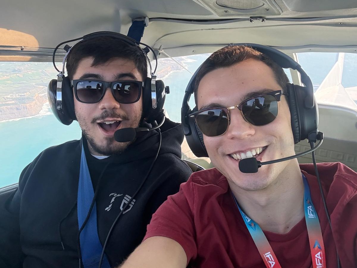 Two passengers smiling in a SkyFuns cockpit above the coastline